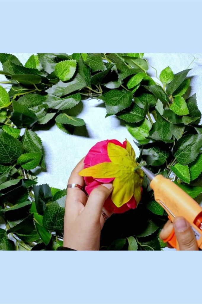 Once the green leaves are fixed we start attaching the faux flowers into the wreath