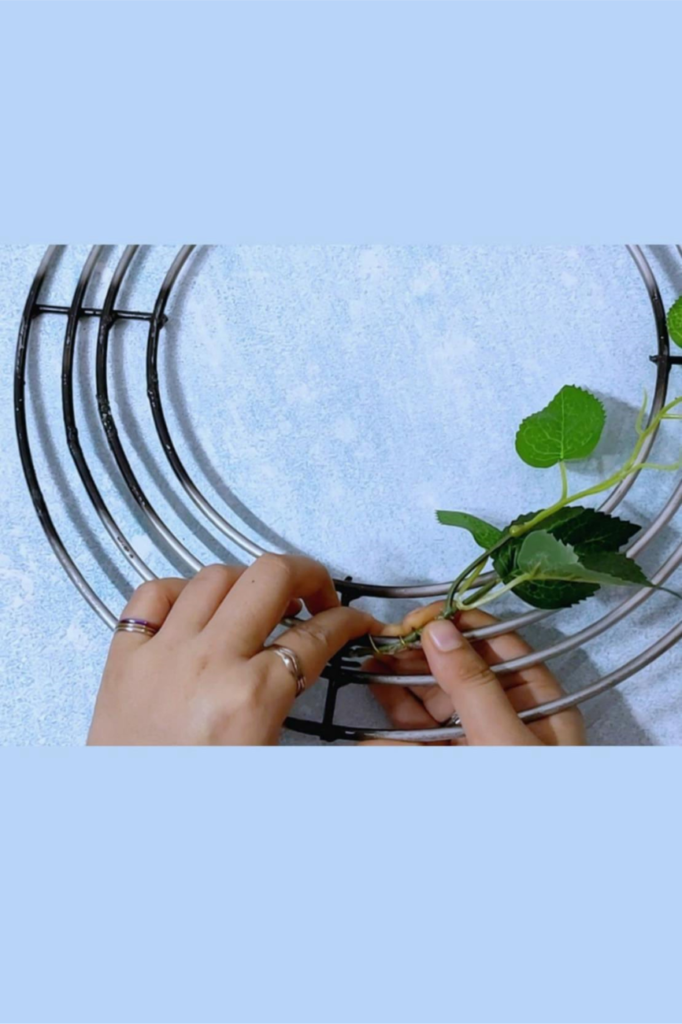 Use the wire to attach the green leaves and branches on the metal wreath frame to settle the base of the crown